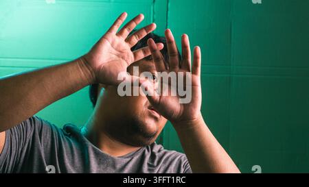 A frightened young indonesian male raises both hands defensively in front of the face, showing a strong reaction of fear, rejection, or self defense a Stock Photo