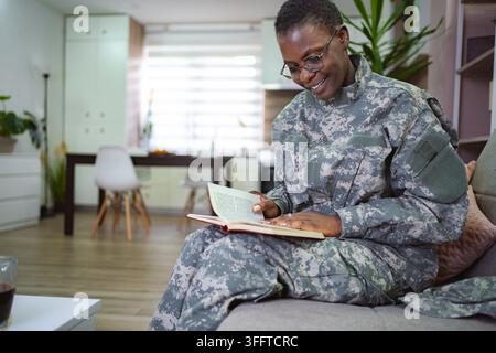 Senior adult in a military uniform enjoys reading a book while sitting on a comfortable sofa in a modern living room Stock Photo