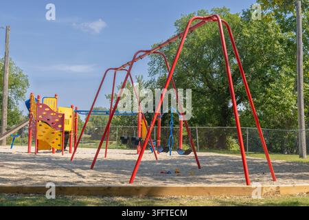 Empty playground with swings, colorful play equipment, gravel surface and scattered toy trucks on a sunny summer day. Stock Photo
