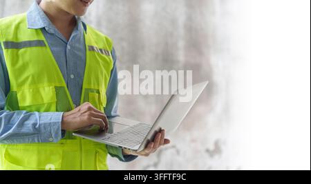 Construction engineer in safety vest typing on laptop with copy space for site management Stock Photo