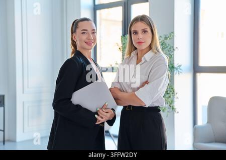 Two confident business women standing looking at camera in modern office Stock Photo