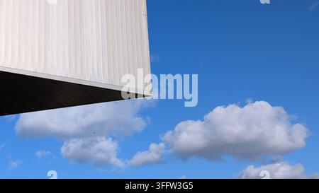 An architectural abstract featuring a sharp building angle juxtaposed against a vibrant blue sky with fluffy white clouds. Stock Photo