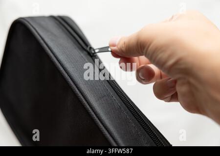 Hands opening black zippered protective case with textured fabric exterior, close-up product detail on light background with copy space. Stock Photo