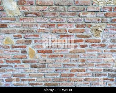 Wall of old antique orange brick of different shades with inserts of different light stones. The gap between the bricks filled with cement is visible. Stock Photo