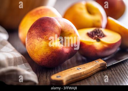 Fresh ripe nectarine and a halved peach arranged on a wooden cutting board with a knife and checkered kitchen towel, evoking summer fruit, rustic cook Stock Photo
