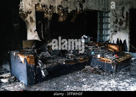 Damaged sofa in a room after a fire with soot-covered walls and charred furniture. Disaster aftermath, property damage, home destruction. HQ photo Stock Photo