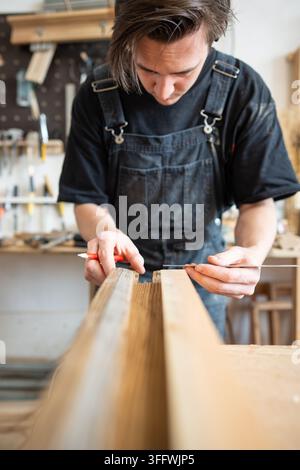 Carpenter making measurements for patch replacement on vintage wooden window frame in repair shop. Stock Photo