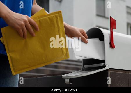 Postal service and mail delivery, person putting letters into a mailbox for shipping and correspondence with yellow padded envelopes in hand Stock Photo