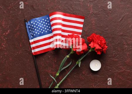 Memorial day tribute, American flag with red carnations and tea light candle for remembrance and patriotism on a dark textured background Stock Photo