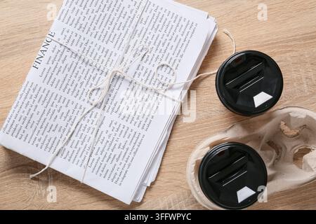 Business news and financial planning, stack of newspapers tied with string and two takeaway coffee cups on a wooden desk for morning work routine Stock Photo