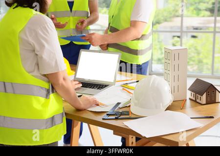 Construction project management and engineering team, architects working on building blueprints with laptop and models in a modern office workspace Stock Photo