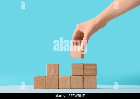 Business strategy and development, hand placing wooden block to complete structure for growth and success concept on a blue background Stock Photo
