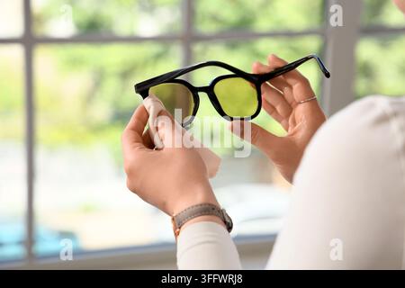 Eye care and vision health, woman cleaning yellow tinted glasses with a microfiber cloth for clear sight and maintenance of optical accessories Stock Photo