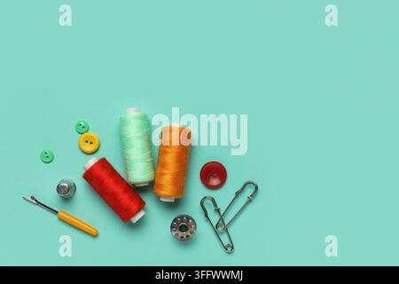 Composition with thread spools, thimble and buttons on mint background Stock Photo