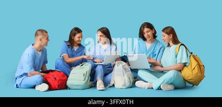 Medical education and nursing students, diverse group of young people in scrubs using laptops and backpacks for collaborative learning on blue backgro Stock Photo
