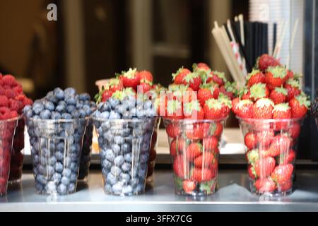 Fresh Strawberries Blueberries and Raspberries Displayed in Clear Plastic Cups at Street Market Stock Photo