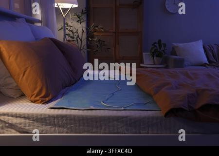 Electric heating pad on bed in dark room Stock Photo