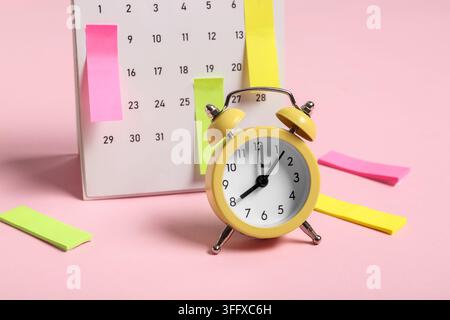 Alarm clock with calendar and sticky notes on pink background. Time management concept Stock Photo