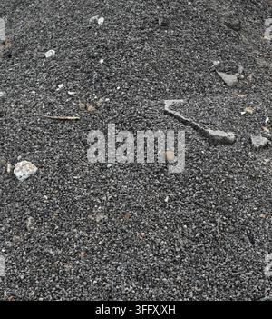 Dark gray asphalt gravel with debris in vertical close-up, showing loose aggregate, mixed gray and tan pebbles, white rocks and asphalt fragments Stock Photo