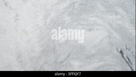 Subtly variegated white granite surface with phaneritic crystalline texture, diffuse gray and white mineral coloration, gentle flowing gray patterns Stock Photo