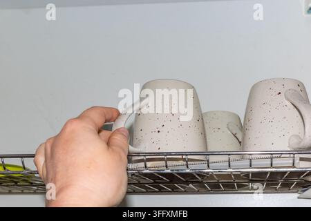 Hand taking mug from built in dish drying rack, space saving kitchen storage and organized home concept. Stock Photo