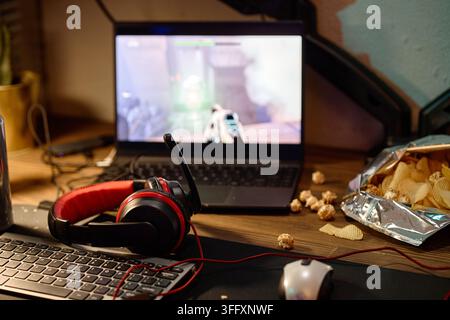 Gaming Setup with Laptop Displaying Video Game and Headset on Desk Stock Photo