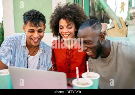 Multicultural startup team enjoys a relaxed outdoor meeting, collaborating over a laptop, having fun Stock Photo