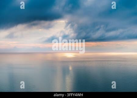 Sunlight breaks through layered clouds over a rugged mountain ridge ...
