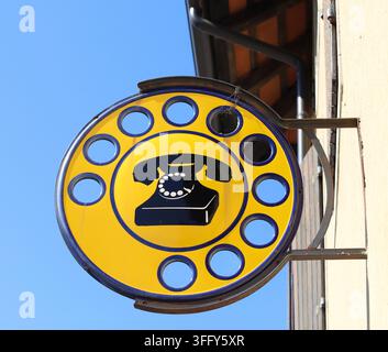 Old public telephone sign with a black rotary dial phone in the middle on round yellow background. Vintage italian signpost hanging to a wall Stock Photo