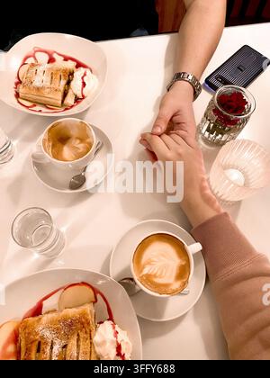 Two hands held together male and female on the table at breakfast with coffee and ice cream cake, date, feelings, top view Stock Photo