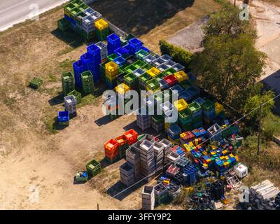 Aerial view of stacks of colorful plastic crates in various shades of blue, yellow, green, and orange arranged in an outdoor storage area in Ortezzano Stock Photo