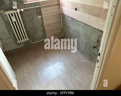 Partially renovated kitchen with newly installed ceramic floor and wall tiles, unfinished plastered walls, exposed plumbing and a traditional radiator Stock Photo