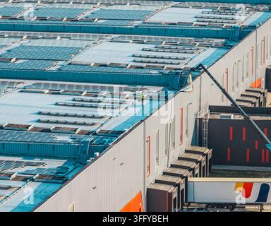 Aerial view of a worker in high-visibility clothing inspecting solar panels on the roof of a large industrial warehouse in Valence, Auvergne-Rhone-Alp Stock Photo