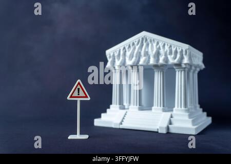 Warning sign and a blurred white classical courthouse model. Legal hazards, judicial risk, regulatory compliance warnings, or constitutional crisis Stock Photo