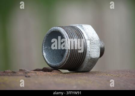 A single galvanized pipe fitting with visible threads sits on a textured, weathered surface, suggesting industrial or plumbing contexts Stock Photo