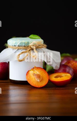 Organic plum preserve with ripe fruits and green leaves on dark background . Stock Photo