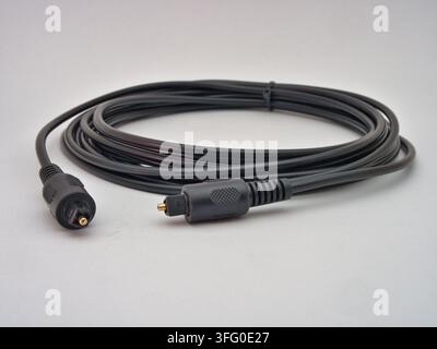 Black TOSLINK Optical Audio Cable - A coiled black TOSLINK optical audio cable with two connectors is isolated on a clean white background, ready for Stock Photo
