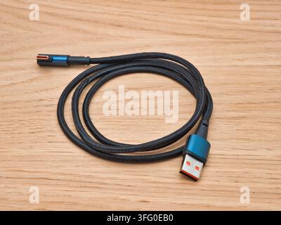 Black Braided USB Cable on Wood Surface - A black braided USB-C to USB-A data and charging cable is coiled on a natural light wooden background, ideal Stock Photo