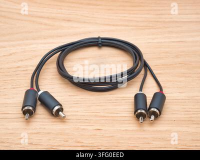 Black RCA Audio Cable on Wooden Backgrou - A black RCA stereo audio cable with two pairs of connectors is neatly coiled and placed on a light natural Stock Photo