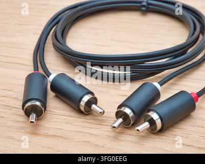Black RCA Audio Cable on Wooden Backgrou - A black RCA stereo audio cable with two pairs of connectors is neatly coiled and placed on a light natural Stock Photo