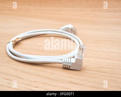 White Ethernet Network Cable on Wood - A coiled white Cat 5e UTP Ethernet network cable with RJ45 connectors lies neatly on a light wood grain surface Stock Photo