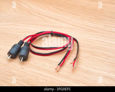 RCA Speaker Wire Connectors on Wood - A pair of black and red RCA audio speaker wire connectors with exposed copper strands rests neatly on a light wo Stock Photo