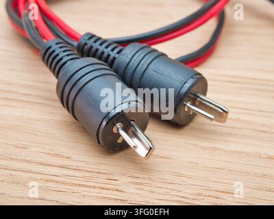 RCA Speaker Wire Connectors on Wood - A pair of black and red RCA audio speaker wire connectors with exposed copper strands rests neatly on a light wo Stock Photo