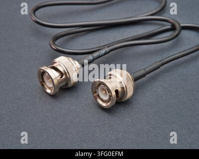 Black Coaxial Cable with BNC Connectors - A close-up view of a black coaxial cable terminated with two silver BNC connectors on a dark gray surface, h Stock Photo