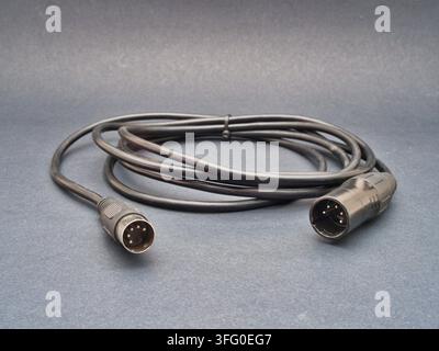 Black Audio Cable with XLR and DIN Conne - A black audio cable with a 5-pin DIN connector and a 3-pin XLR connector lies coiled on a dark grey surface Stock Photo