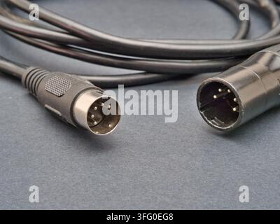 Black Audio Cable with XLR and DIN Conne - A black audio cable with a 5-pin DIN connector and a 3-pin XLR connector lies coiled on a dark grey surface Stock Photo