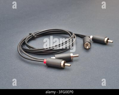 RCA Audio Cable on Dark Background - A black stereo RCA audio cable with red and white connectors is neatly coiled and secured on a dark gray surface. Stock Photo