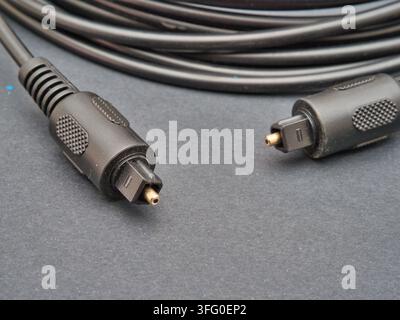 Black Optical Audio Cable - A black optical audio cable with TOSLINK connectors, coiled neatly on a dark gray background, ready for high-fidelity digi Stock Photo