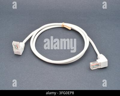 White Ethernet Cable with RJ45 Connector - A white twisted-pair Ethernet cable with right-angle RJ45 connectors lies coiled on a plain gray background Stock Photo