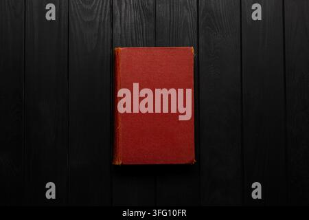 Old closed book with red hard cover on dark wooden background. Stock Photo